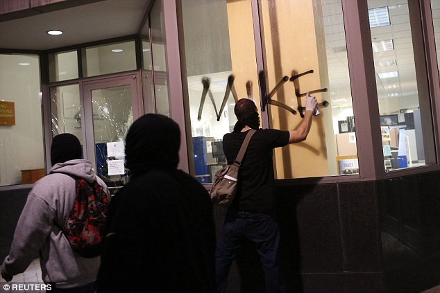 A demonstrator vandalizes a window during a demonstration in Oakland, California