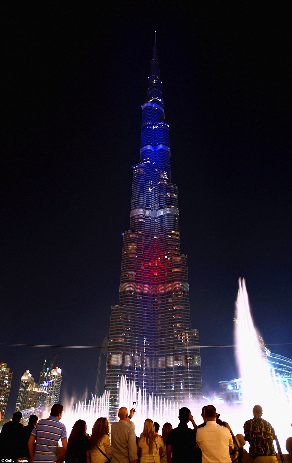 Solidarity: Locals and tourists in Dubai stand together in the centre of the city as the Burj Khalifa is lit up in the colours of the French flag